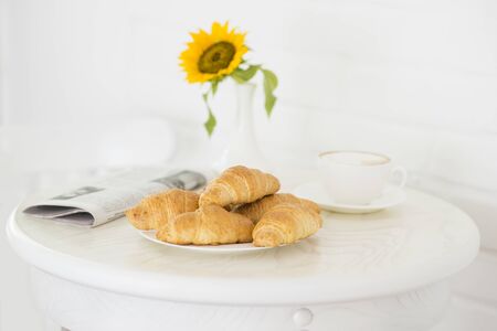 Croissant with a cup of coffee. Newspaper and yellow flower on the table