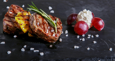 Beef  medalions, ananas,    grapes  on  black plateの写真素材