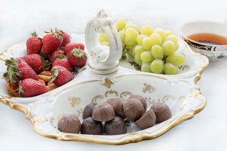 Chocolates , grapes and strawberries in  combined plate and  cup of teaの写真素材