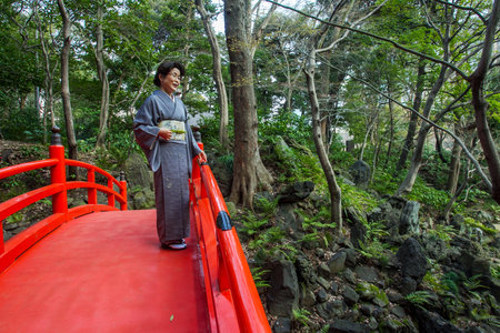 03-22-2015 Tokyo. Japanese woman in kimono watching and smiling on nature o red japanese bridge in Koishikawa Korakuen Gardenのeditorial素材