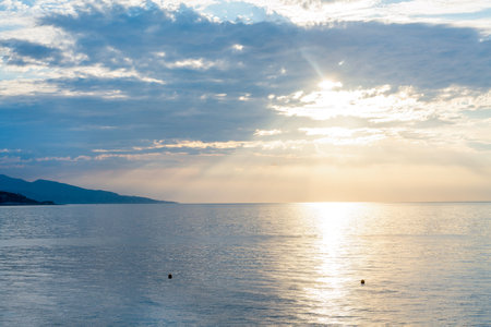 Sunrise in Monaco (Monte Carlo) - Partly cloudy in the morning and a wonderful line of mountain slope on Cap Martin. Blue water and yellow sun!の写真素材