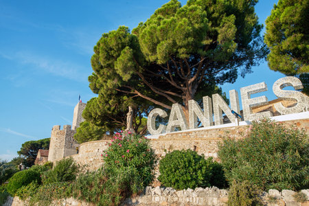 Sign "Cannes" next to Eglise Notre-Dame d'Esperance on hill . There luxury pine trees and old statueの写真素材