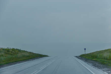 Car road in the rain, disappearing into fog