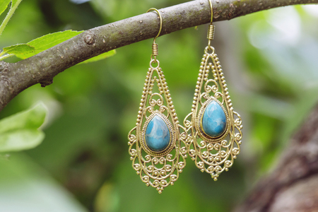 brass metal earrings with natural mineral larimar stone hanging on tree branchの写真素材