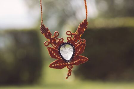 Boho style macrame necklace with natural mineral gemstone on green outdoor bokeh background