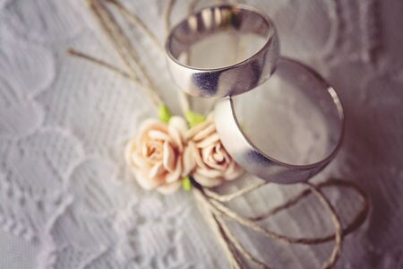 Wedding ring on lace pillow with sweet artificial small rose blossomsの写真素材