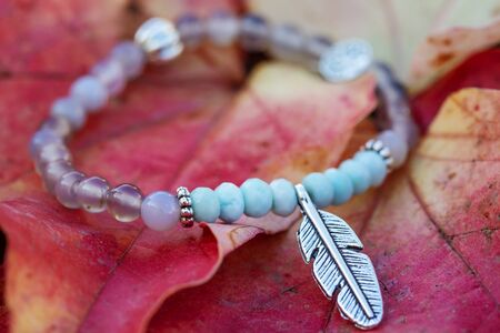 Metal feather pendant mineral stone bracelet on autumn background