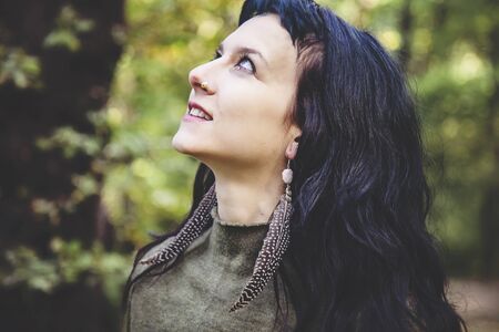 Portrait of beautiful young woman with feather earring in forest
