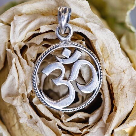 Sterling silver pendant in shape of om symbol in cyrcle placed on dried rose