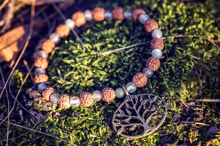 Metal tree pendant with natural seed and labradorite mineral stone beads on yoga bracelet in the forest backgroundの写真素材