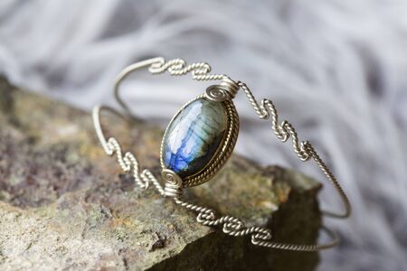silver metal wire elegant bracelet with labradorite stone on rocky backgroundの写真素材