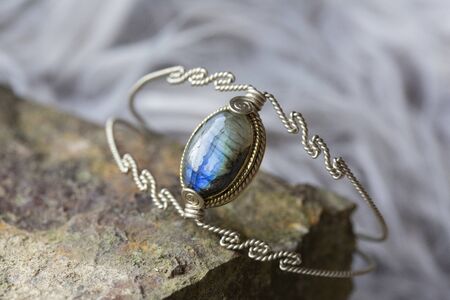 silver metal wire elegant bracelet with labradorite stone on rocky backgroundの写真素材