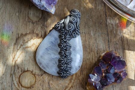 Beautiful moon stone gemstone pendant on wooden backround with amethyst drusesの写真素材