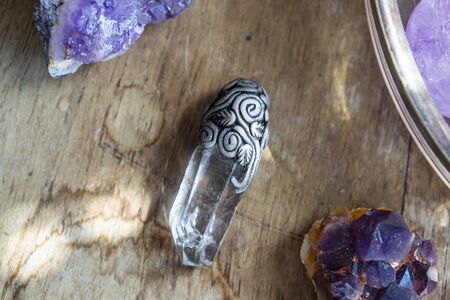 Beautiful crystal quartz gemstone pendant on wooden backround with amethyst drusesの写真素材