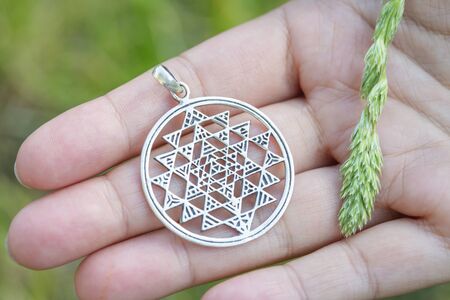 Sterling silver pendant in the shape of sri yantra sacred geometry on female handの写真素材