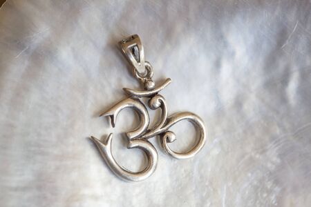 Sterling siver pendant in the shape of om on white shell background