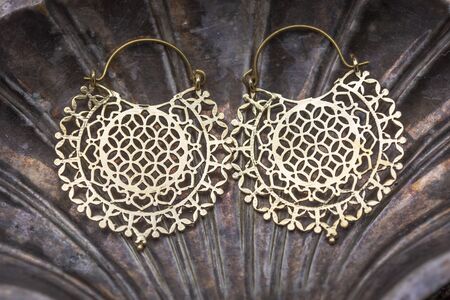 Brass metal earrings with flower of life on decorative silver shell background