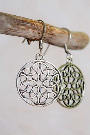 Brass metal earrings in ornamental shape hanging on neutral backgroundの写真素材