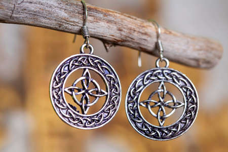 Brass metal earrings in ornamental shape hanging on neutral backgroundの写真素材
