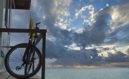 Sunrise on the beach with a bicycle; the lifeguard cottage with a bicycle and yellow flag at a beach in Playa del Carmen, Mexico. In the background the Caribbean sea and the cloudy skyの写真素材