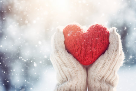 Hands in mittens with knitted heart at snowy winter backgroundの素材