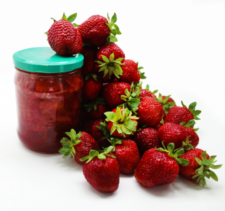 Ripe red strawberries and a jar of strawberry jam on a white background.