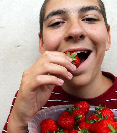 Funny young boy eating a ripe strawberryの写真素材