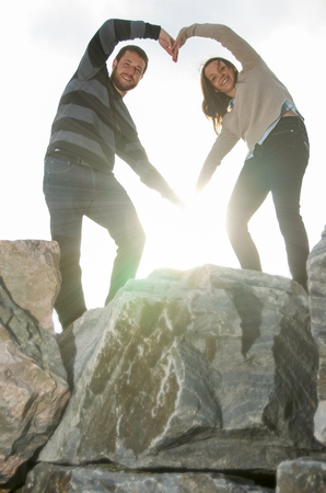 Young couple standing on large rocks making heart shape  with sun burst where their hands meetの写真素材