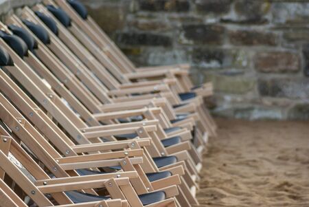 A row of suspended empty deck chairs in rows lined up in order on the beach in the sand, a row of empty chairs laid out in rows on the beach in the sandの写真素材
