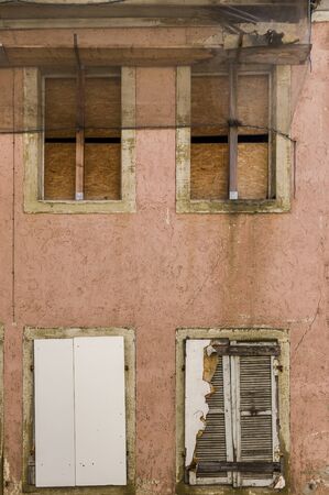 Facade of abandoned, dilapidated house with 4 boarded windows, shutters, boards and flow as...