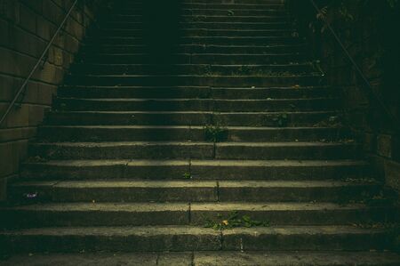 Wide staircase in a park made of natural stone with a handrail made of rusted steel in the dim light with a creepy and scary aura like in a thrillerの写真素材