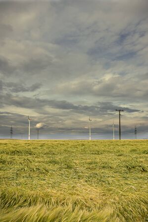 Dramatic cloud sky over cornfield with dark rain clouds and power lines and wind turbinesの写真素材