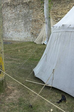Reenactment of a medieval scene against the historical backdrop of an old city wall, village with tents of various designs with details of fabrics and pegs, ropes and bracing, view of tentsの写真素材