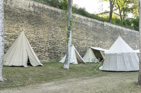 Reenactment of a medieval scene against the historical backdrop of an old city wall, village with tents of various designs with details of fabrics and pegs, ropes and bracing, view of tentsの写真素材