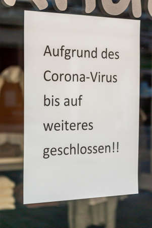 Shop window of a shop with a sign "Closed because of the Corona virus", in German, with displays and the reflection of the surroundings in blur at the time of the Corona Covid-19 pandemic in March 2020のeditorial素材