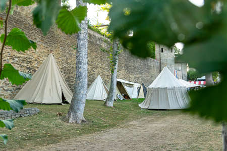 Reenactment of a medieval scene against the historical backdrop of an old city wall, village with tents of various designs with details of fabrics and pegs, ropes and bracing, view of tentsのeditorial素材
