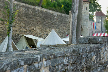 Reenactment of a medieval scene against the historical backdrop of an old city wall, village with tents of various designs with details of fabrics and pegs, ropes and bracing, view of tentsのeditorial素材