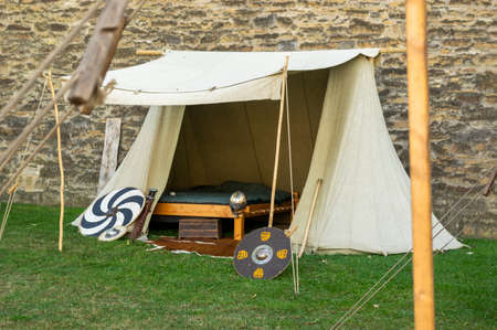 Medieval scene against the historical backdrop of an old city wall, village with tents of various designs, view of tents, village square with utensils and containers, furniture, wooden storage and transport cartのeditorial素材