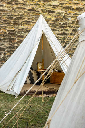Reenactment of a medieval scene against the historical backdrop of an old city wall, village with tents of various designs with details of fabrics and pegs, ropes and bracing, view of tentsのeditorial素材