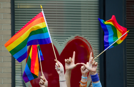 Hands waving gay flags in front of a big red heartの写真素材