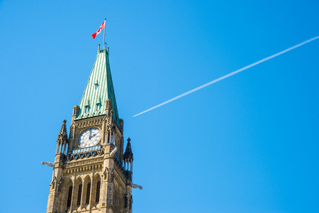 Canadian Parliament Peace tower in Ottawa, with a plane over the blue sky and a white smoke trailの写真素材