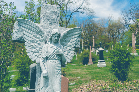 Angel before a cross statue in a cemetary, with a vintage effect.の写真素材
