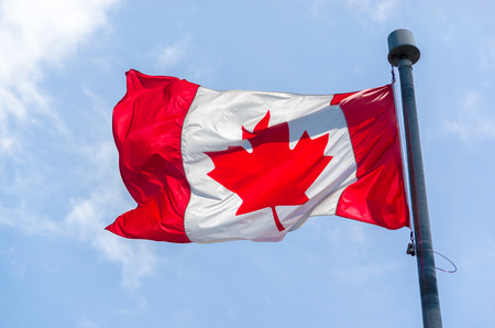 Canadian Flag in the wind over blue sky with cloudsの写真素材