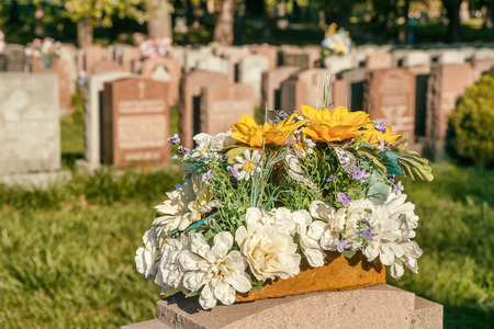 Flowers in a cemetery with headstones in the background at sunsetの写真素材