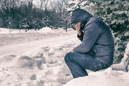 Man sitting on bench in a forest in winter with snow on the groundの写真素材