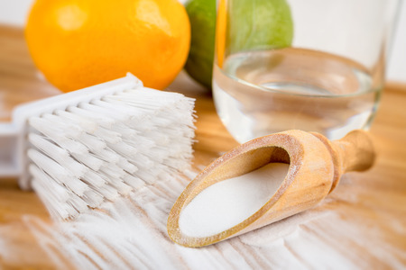 Baking soda in a wooden spoon next to a brush, two lemons and a glass of waterの写真素材
