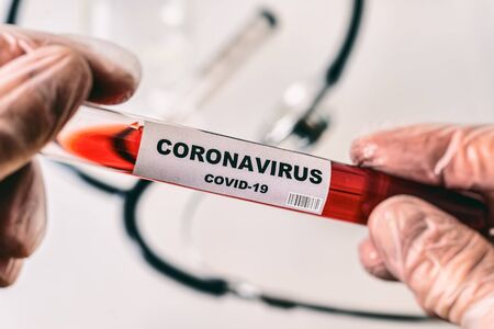 Hands in gloves holding tube with Coronavirus Covid-19 label, filled with red liquid (artistic rendering)の写真素材