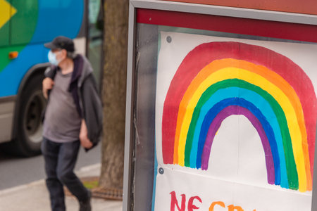 Montreal, CA - 16 May 2020: Man with face mask for protection from COVID-19 walking near rainbow drawingのeditorial素材