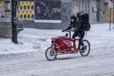Montreal, CA - 2 February 2021: Delivery courier on a bike rides under the snowのeditorial素材