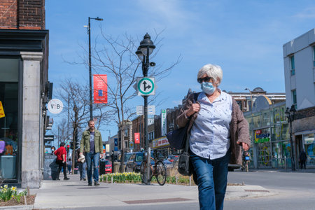 Montreal, CA - 11 April 2021: Pedestrian with face mask for protection from COVID-19 walking down the streetのeditorial素材